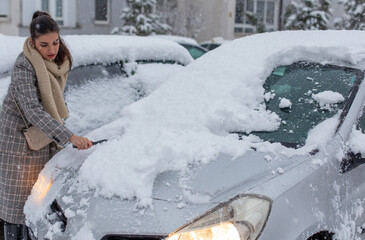 Portrait of a young girl cleaning a car from snowfall.