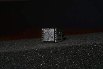 Anillo de plata con iniciales sobre una espuma negra y un fondo negro