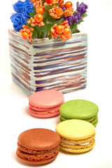 Composition with sweet tasty macaroons and vase with flowers on white background.