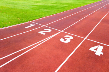 Aerial view of sports stadium with red running tracks with numbers on it and green grass football field.