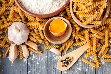 wholemeal raw pasta fusilli type, flour and egg, garlic on an old table	
