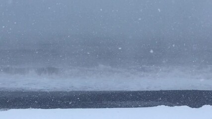 View of heavy snowing conditions on beach with crashing waves in background