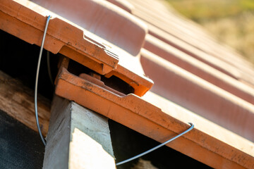 Closeup of metal montage anchor for installation of yellow ceramic roofing tiles mounted on wooden boards covering residential building roof under construction.