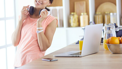 Pretty woman on the phone using laptop at home in the kitchen