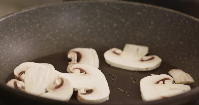 Sliced champignons mushrooms falling into frying pan. Close up