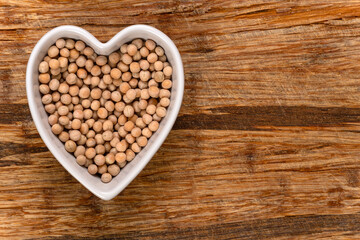 Whole yellow peas in a heart-shaped bowl background and texture. Top view.