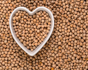 Whole yellow peas in a heart-shaped bowl background and texture. Top view.