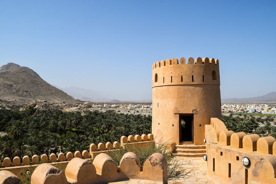 One tower and the walls of Nakhal Fort in a beautiful sunny day. Outside its walls, there are a lot of palm trees. Nakhal, Oman.
