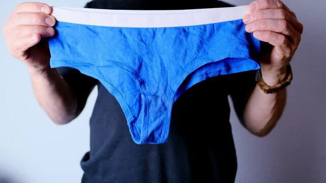 man holding blue women's panties in his hands, knitted underwear, concept of comfortable clothes, female intimate problems