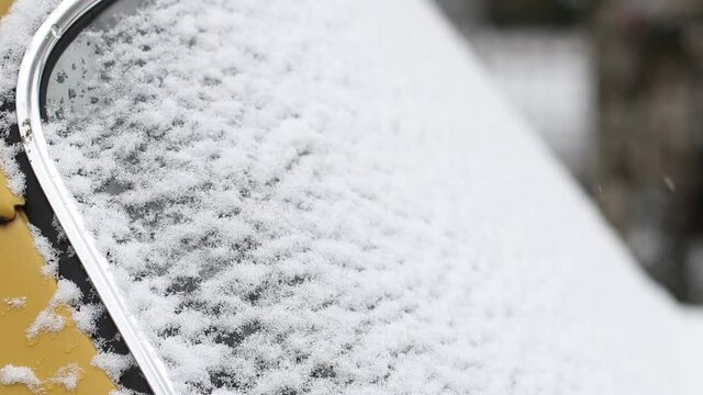 Ice and snow melting from a yellow vintage car window in winter, closeup exterior view