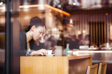 Worried businesswoman at a cafe, having coffee and looking at tablet.