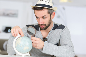 man looking at globe through a magnifying glass