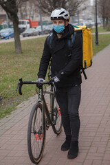 Fototapeta premium Vertical shot of a male courier wearing medical face mask and thermo delivery backpack, walking with bicycle