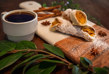 Cup of coffee and pumpkin cannoli sprinkled with powdered sugar on a marble and wood cutting board...