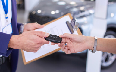 Car salesman sells a car to happy customer in car dealership and hands over the keys