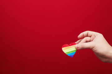 Lgbt valentine's day concept, rainbow heart in hand on red background, copy space