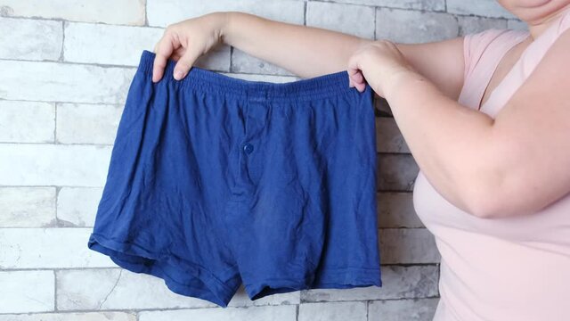 woman holding blue men's underpants in her hands, knitted underwear, concept of comfortable clothes, female intimate problems, scandal in the Russian Federal Security Service