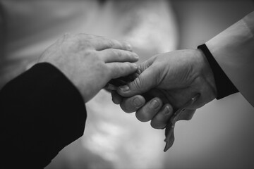 A grayscale closeup of the groom touching the priest's cross