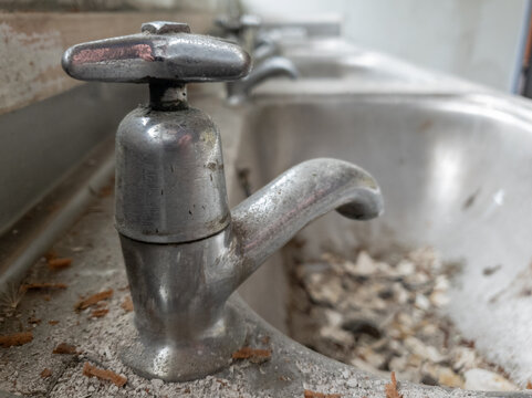Close up of a dirtly chrome tap in a row of neglected wash basins.