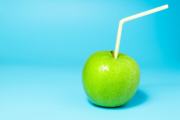 Fresh green apple with water drops and straw on cheerful blue background.