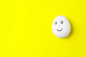 One white chicken egg with smiling face on yellow background with copy space.