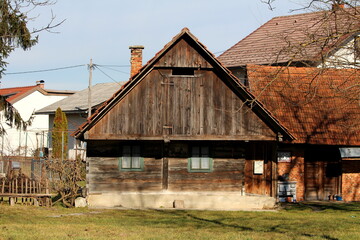 Side view of small old wooden family house with green frame windows next to red brick outdoor building surrounded with freshly cut grass and other houses in background on cold sunny winter day