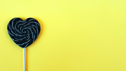 Black candy heart-shaped on yellow background card flatly