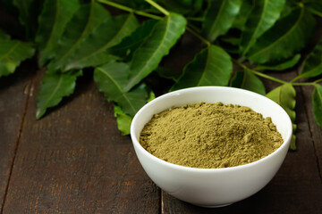 neem powder in white bowl and neem leaf on wooden background.