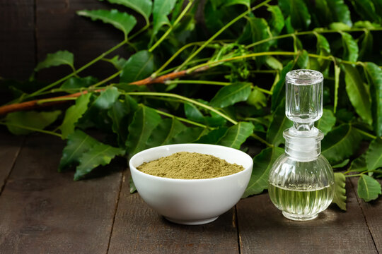 neem powder in white bowl with neem oil in glass bottle on wooden background.