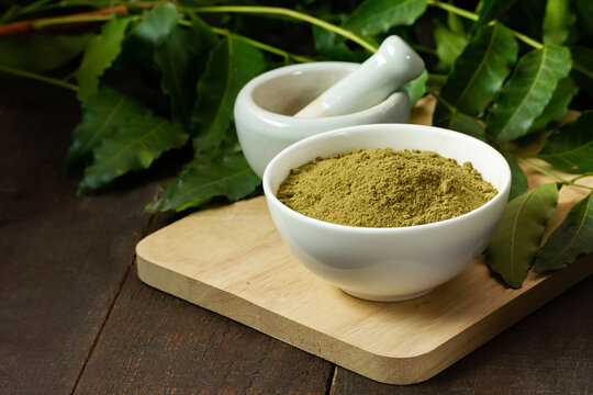 neem powder in white bowl with neem leaf and white mortar and pestle on wooden background.