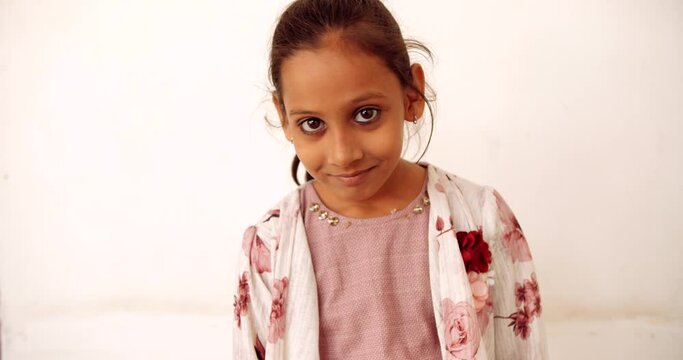 Slow-motion portrait of a young girl child standing against white background happy smiling looking at camera making facial expression hand gestures and sign- shy smug naughty