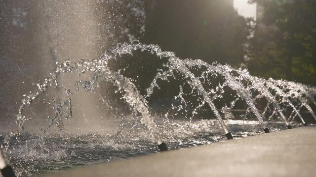 Beautiful fountain on a bright sunny day in slow motion. Jets of water sparkle in the sun. Bright splashes slowly spread to the sides.