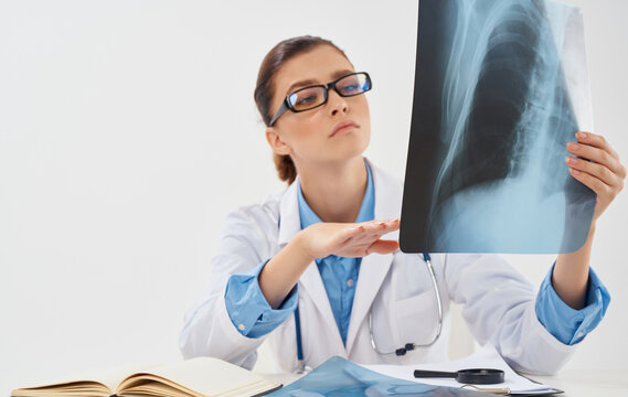 A nurse in glasses with an X-ray in her hands sits at the table and documents