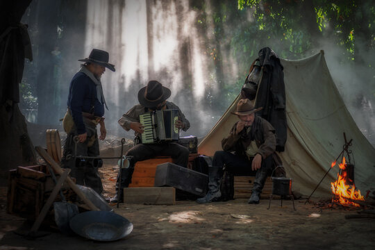 Three Cowboys Are Relaxing Playing And Listening Music In Outdoor Camping With The Accommodation Tent.