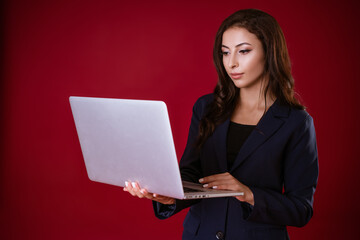 Young woman decides business cases in a laptop on a red studio background.