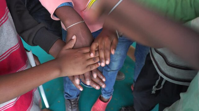 Arm stacked together one by one in unity and teamwork. Many hands getting together in the center of a circle. Close up outdoor shot. Many african children hands connecting, Tanzania, East Africa