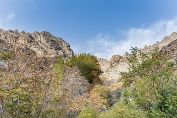 Fototapeta na wymiar Tochal mountain ridge with rocks and trees in autumn against blue sky, Tehran, Iran. Tochal is a popular recreational region for Tehran's residents
