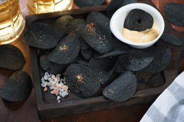 Close-up of black potato chips and dip on a wooden serving tray with beer mugs in the background