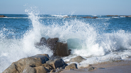 Ocean spray splashing into the air as waves splash over rocks on the beach
