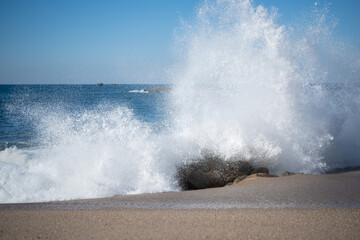 Big, powerful waves splashing against rocks on the beach, sending ocean spray into the air