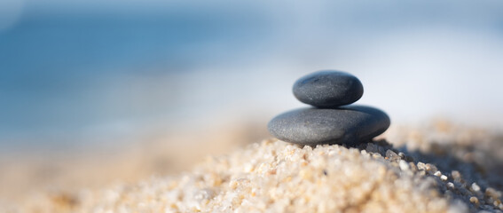 Two smooth black pebbles balanced on sandy beach. Soft focus with shallow depth of field.