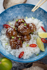 Obraz premium White rice with pork meatballs in teriyaki sauce served in a blue plate, vertical shot, close-up
