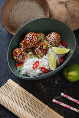 Green bowl with asian-style rice and pork meatballs in sweet and sour sauce, vertical shot on a dark brown stone surface