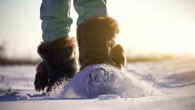 A woman in high fur boots walks in the snow. Slow motion