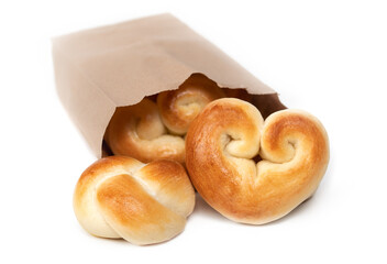 Bread hearts and bread knots in a bag. Single portion yeast bread buns. Concept for valentines day or baking with love. Traditional Swiss butter bread called Zopf or Challah. Isolated on white. 