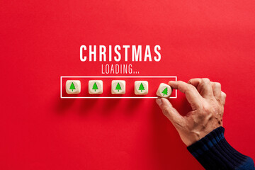Male hand putting wooden cubes with tree icons in Christmas loading bar on red background. Christmas countdown