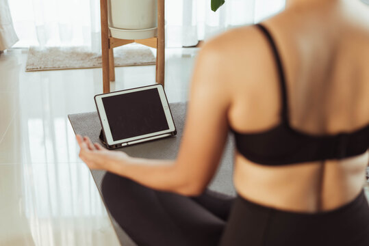 Woman practicing yoga online at home. Fit woman doing yoga online on video call in tablet.