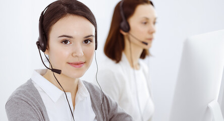 Call center. Casual dressed woman working in headset with diverse colleagues at office. Business...