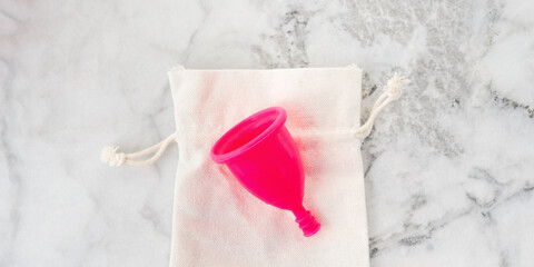 Pink menstrual cup on its storage cotton bag on marble table. Zero waste concept for female hygiene products. Banner