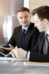 Businessman using tablet computer and work together with his colleague in sunny office. Unknown business people at meeting. Teamwork and partnership concept